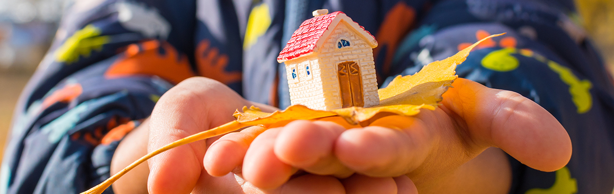 Child holding toy house in cupped hands