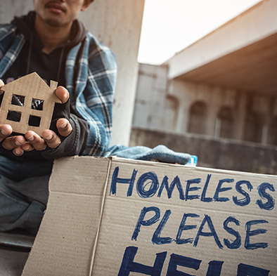 homeless person holding cutout of a house with a  help sign